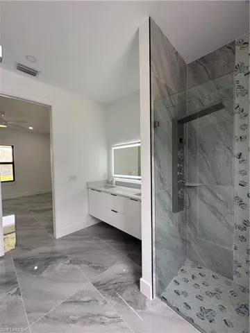 Full bath with marble look tile flooring, a tile shower, vanity, and a ceiling fan