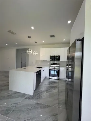 Kitchen with modern cabinets, a peninsula, range, white cabinetry, and refrigerator