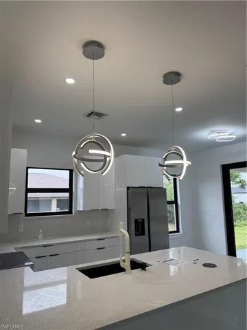 Kitchen with fridge, modern cabinets, white cabinets, hanging light fixtures, and light stone countertops