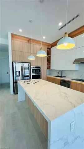 Expansive kitchen island with a stone finish countertop, wood-finish cabinetry, built-in stainless steel appliances, recessed lighting, and pendant fixtures