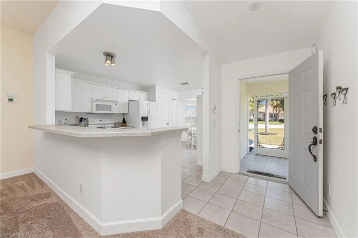 Kitchen with white cabinetry, light tile patterned floors, white appliances, and kitchen peninsula