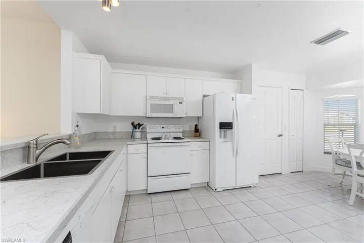 Kitchen with sink, white appliances, white cabinets, and light tile patterned flooring