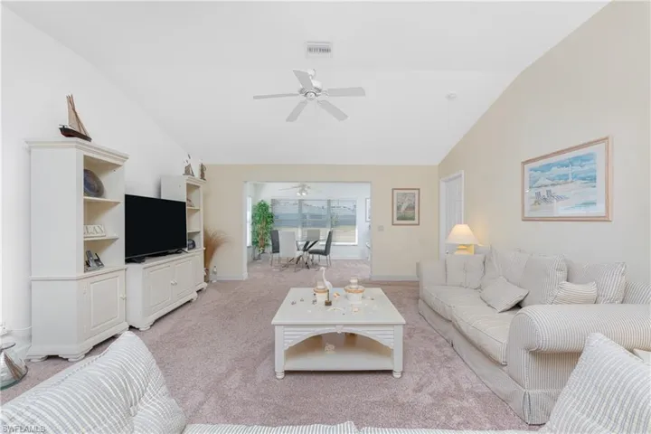 Carpeted living room with ceiling fan and high vaulted ceiling