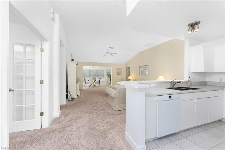 Kitchen with sink, white dishwasher, kitchen peninsula, light colored carpet, and white cabinets