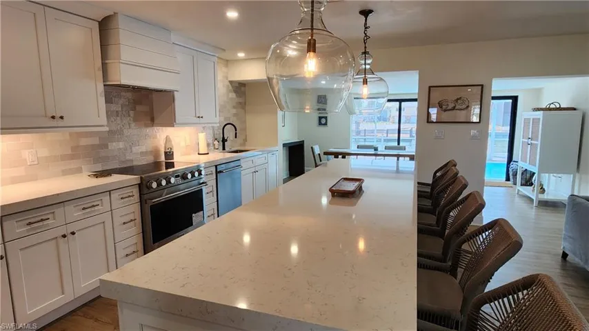Kitchen featuring custom range hood, 2.5" quartz countertops, high end range, decorative backsplash, and pendant lighting