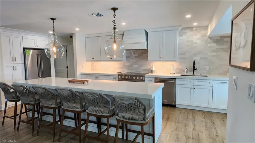 Kitchen with custom range hood, tasteful backsplash, LVP flooring, an island that seats 6, and high quality appliances