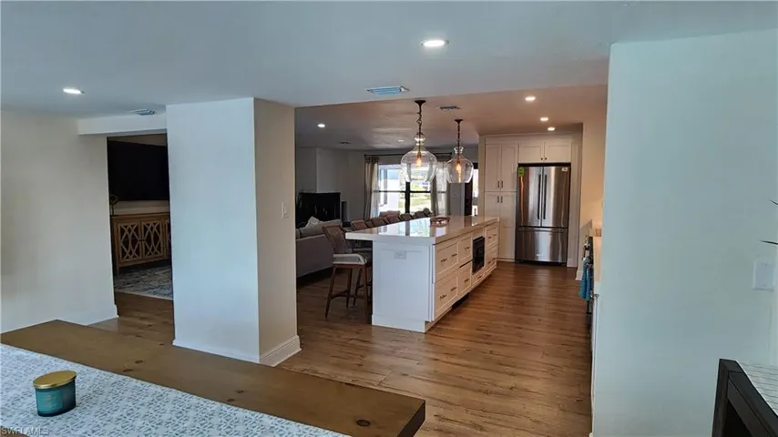 Kitchen featuring stainless steel fridge, pendant lighting, LVP floors, a kitchen island, and white shaker cabinetry