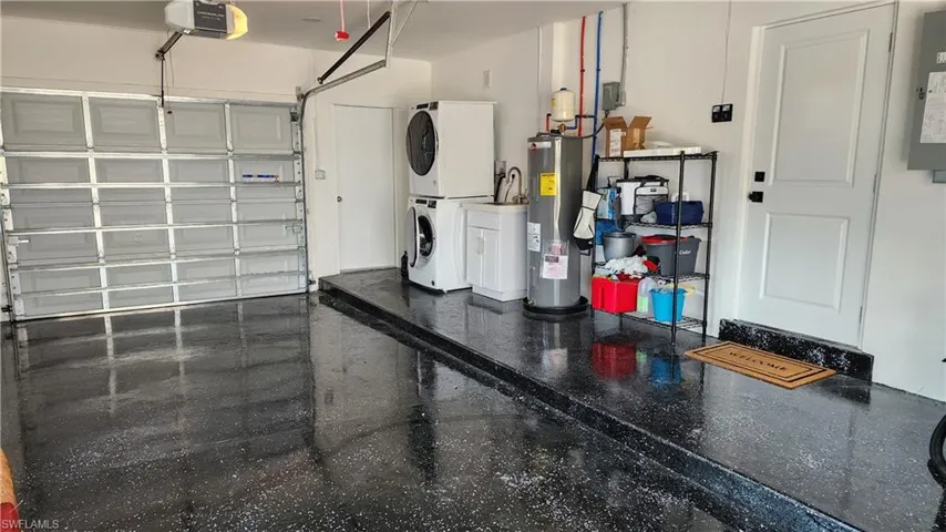 Garage with electric water heater, a garage door opener, and stacked washer / drying machine and utility sink