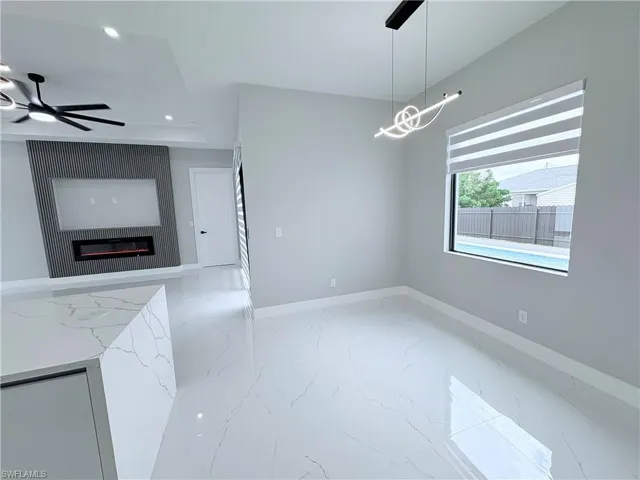 Unfurnished dining area with ceiling fan, a glass covered fireplace, light marble finish floors, and recessed lighting