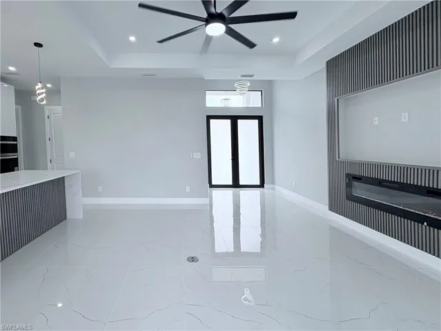 Empty room with light marble finish flooring, recessed lighting, a tray ceiling, a ceiling fan, and french doors