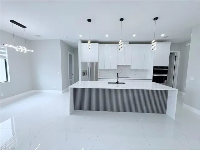 Kitchen with light stone counters, stainless steel appliances, white cabinetry, decorative light fixtures, and a large island