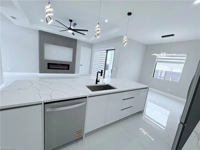 Kitchen with light stone counters, modern cabinets, white cabinets, stainless steel appliances, and a raised ceiling