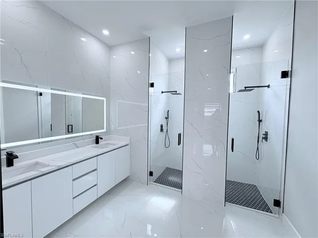 Bathroom featuring double vanity, a marble finish shower, recessed lighting, stone wall, and light marble finish flooring