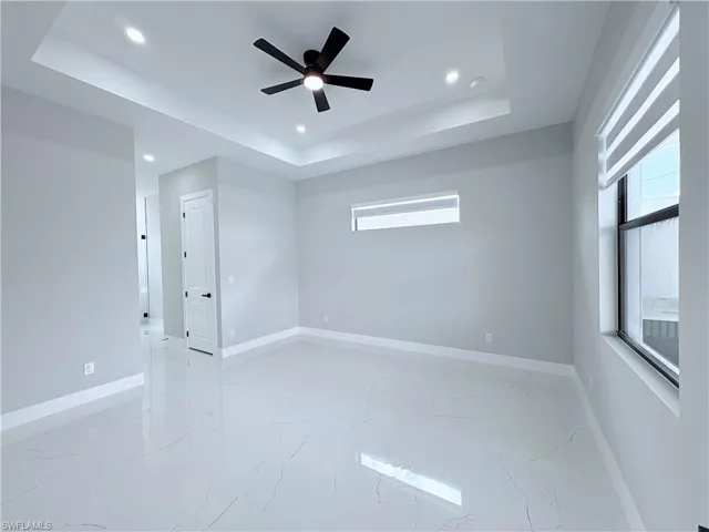 Spare room with plenty of natural light, ceiling fan, light marble finish floors, a raised ceiling, and recessed lighting