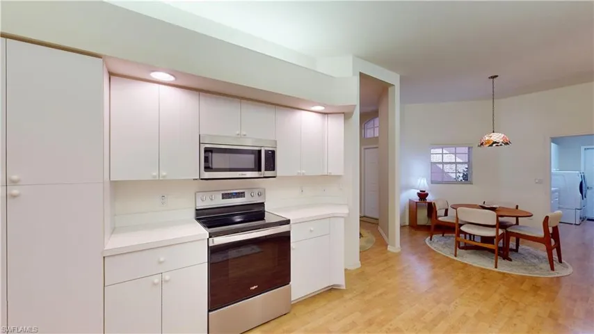 Kitchen featuring stainless steel appliances, light countertops, pendant lighting, washer / clothes dryer, and light wood-style flooring