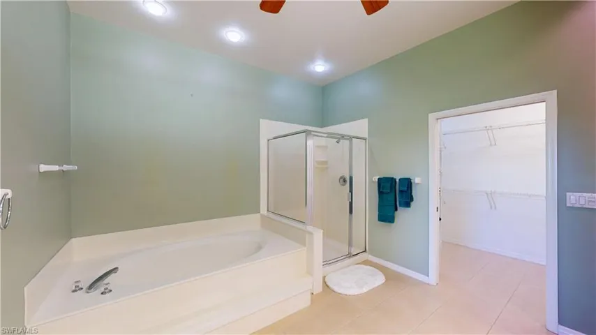 Bathroom with a spacious closet, a garden tub, a stall shower, light tile patterned floors, and ceiling fan