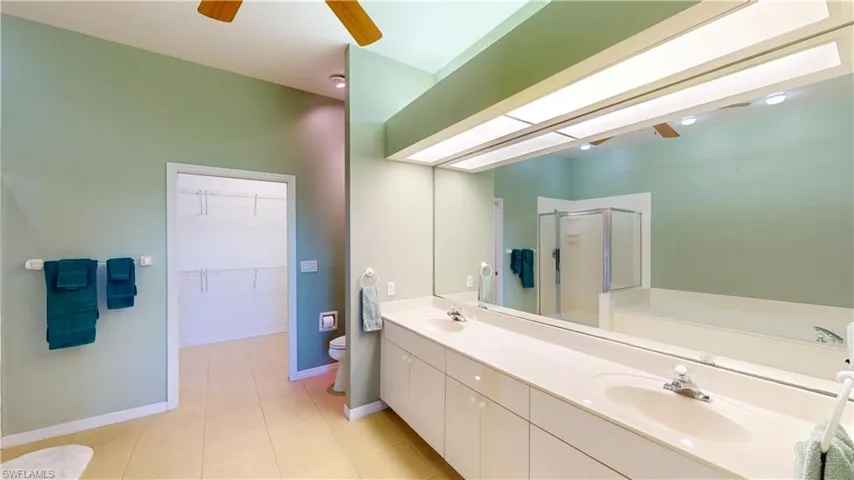 Bathroom featuring a spacious closet, ceiling fan, a shower stall, a bath, and double vanity