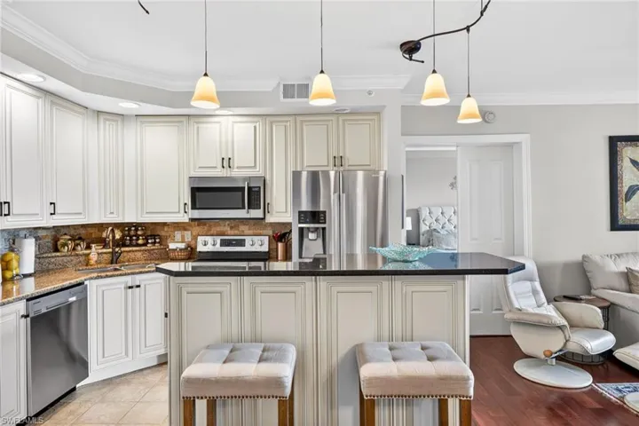 Kitchen featuring ornamental molding, decorative backsplash, a breakfast bar area, stainless steel appliances, and dark stone countertops