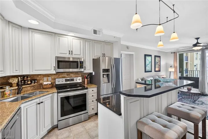 Kitchen with ornamental molding, stainless steel appliances, a kitchen island, a breakfast bar, and dark stone countertops