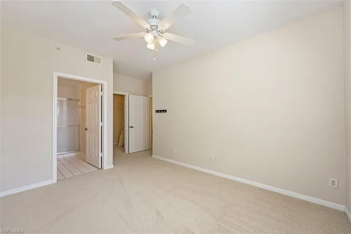 Unfurnished bedroom featuring light colored carpet, a spacious closet, a closet, ceiling fan, and ensuite bathroom