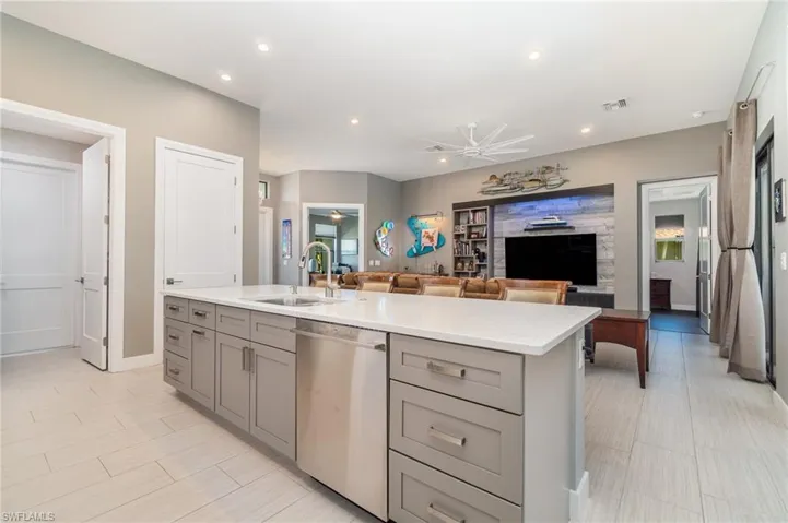 Kitchen island featuring an island with gray cabinets open to great room with sink, dishwasher