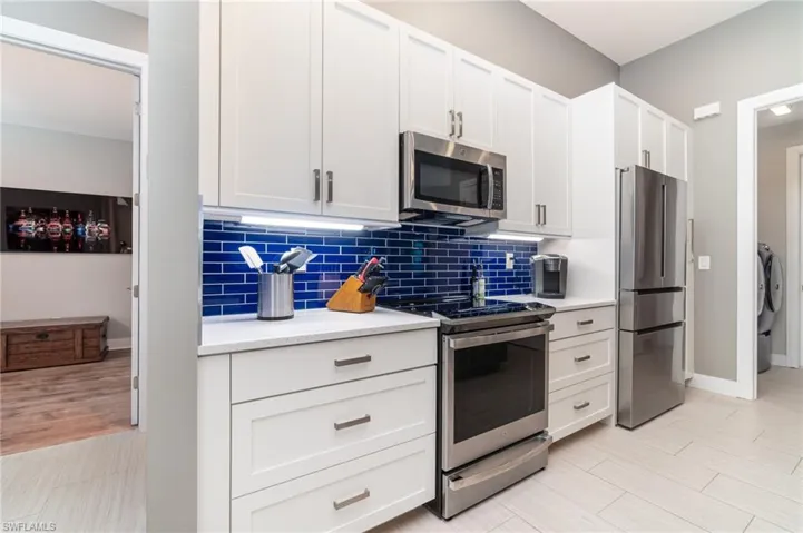 Kitchen with decorative backsplash, white cabinetry, stainless steel appliances
