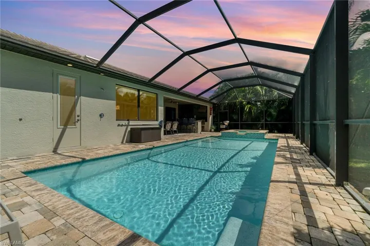 Pool at dusk featuring a lanai, an in ground hot tub, and a patio area