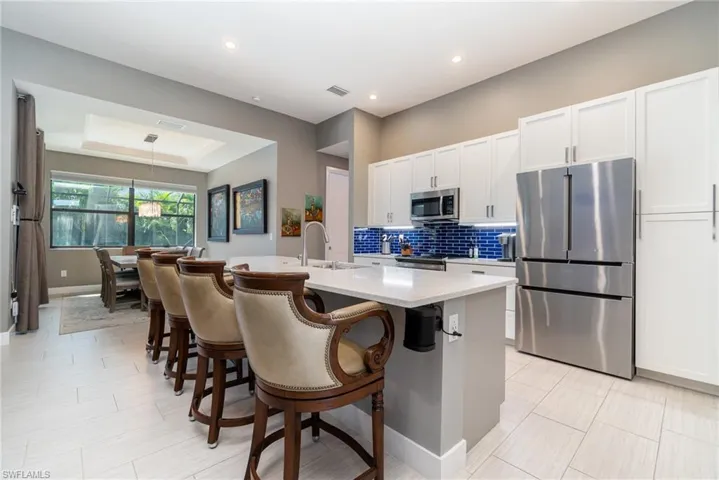 Kitchen featuring a center island with sink, white and gray cabinetry, stainless steel appliances, and tiled backsplash