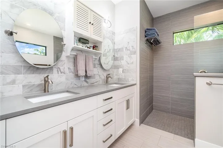 Bathroom featuring backsplash, tile patterned floors, vanity, and tiled shower
