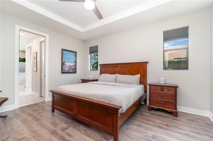 Primary bedroom with connected bathroom, a tray ceiling, ceiling fan, wood flooring, and ornamental molding