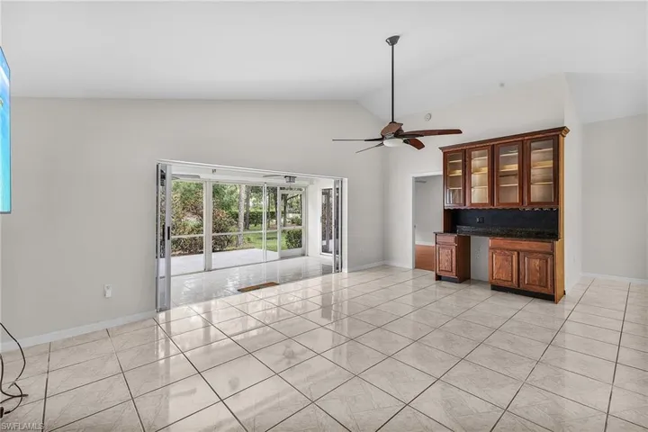 The spacious living room features a high vaulted ceiling, with a custom built-in wood bar with glass front cabinets and room for beverage/wine cooler.