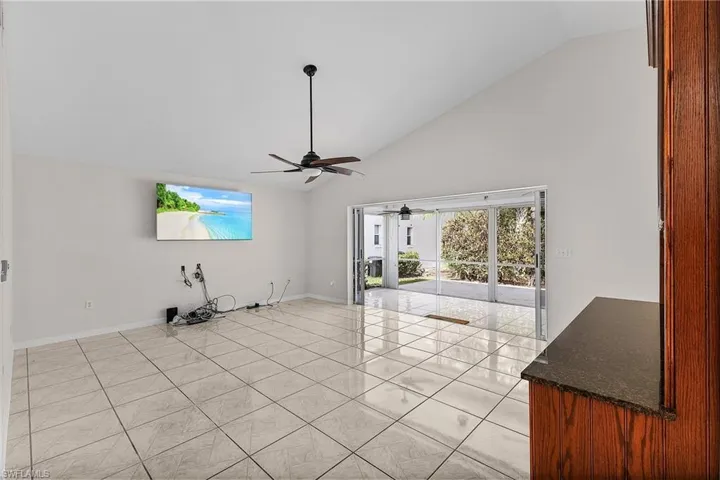 The great room has been freshly painted and features tile flooring, high vaulted ceiling with a fan, a large tv, sliding doors that stack back and access the screened lanai and adjoining patio.