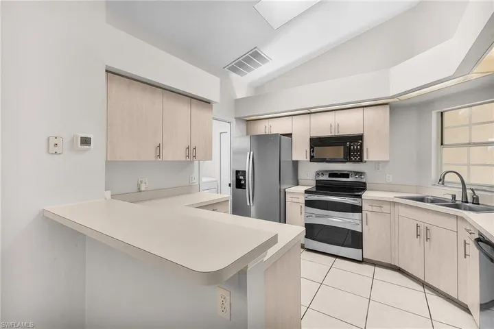 Kitchen featuring appliances with stainless steel finishes, ample cabinetry vaulted ceiling, light countertops. A  skylight and window over the sink provide lots of natural light.