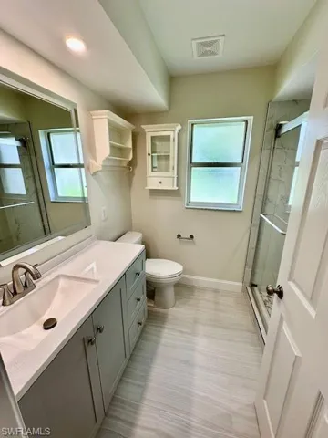 Updated guest bath boasts a raised vanity with solid surface countertop, modern mirror that lights up and de-fogs, beautiful tile flooring, glass-enclosed shower with river stone tile floor, and a new comfort-height commode.