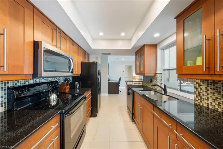 Kitchen featuring black appliances, brown cabinets, dark stone countertops, and a sink