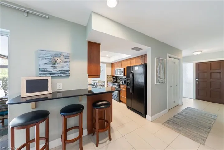 Kitchen with black fridge with ice dispenser, stainless steel microwave, a raised ceiling, dark countertops, and electric range