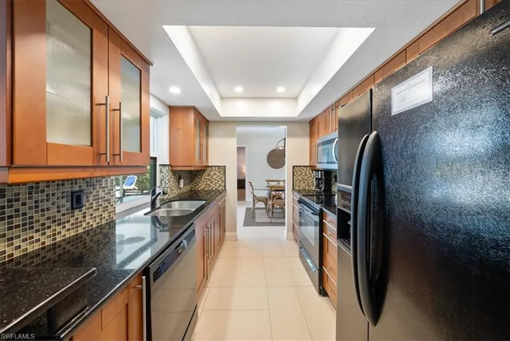 Kitchen featuring a sink, brown cabinetry, a raised ceiling, black appliances, and recessed lighting