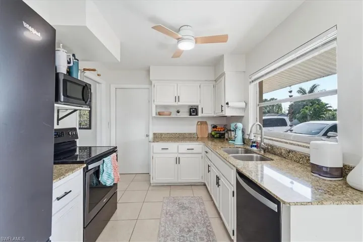 Kitchen featuring electric stove, freestanding refrigerator, open shelves, light stone counters, and white cabinetry