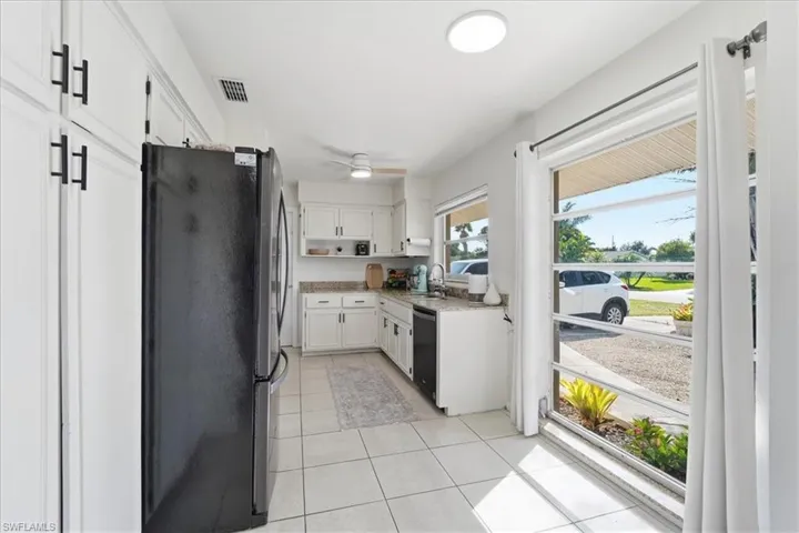 Kitchen featuring white cabinetry, freestanding refrigerator, light tile patterned flooring, and black dishwasher