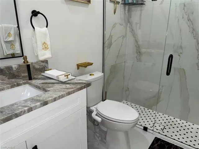 Bathroom with vanity, toilet, and a marble finish shower