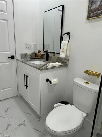 Half bath with vanity, toilet, and marble finish floor