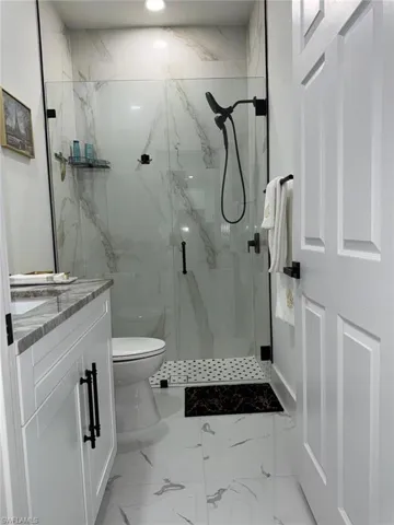 Full bathroom with vanity, toilet, marble finish floor, and a marble finish shower
