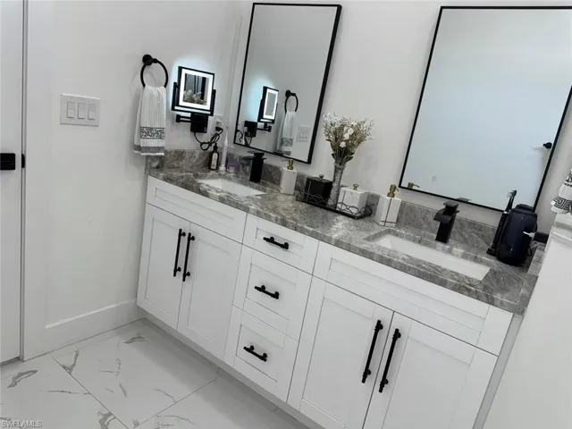 Full bathroom featuring double vanity, marble finish floor, baseboards, and a sink