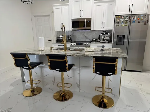 Kitchen featuring marble finish floor, a sink, stainless steel appliances, decorative backsplash, and light stone countertops