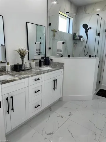 Bathroom with double vanity, marble finish floor, a marble finish shower, and a sink