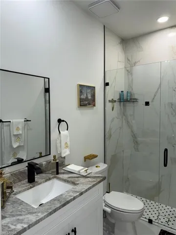 Full bath with a marble finish shower, toilet, marble finish floor, and vanity