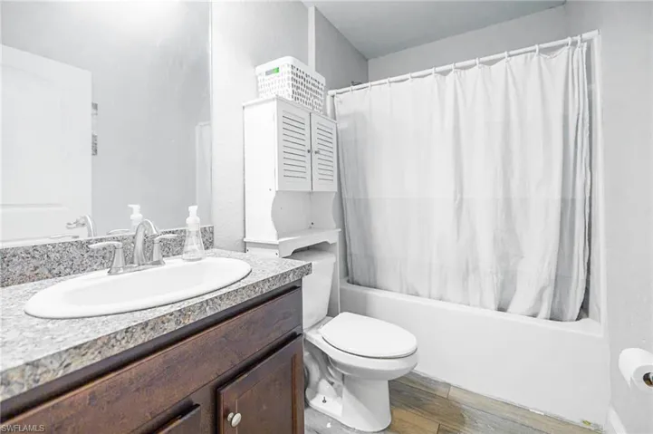 Full bathroom with vanity, toilet, shower / bathtub combination with curtain, and hardwood / wood-style flooring