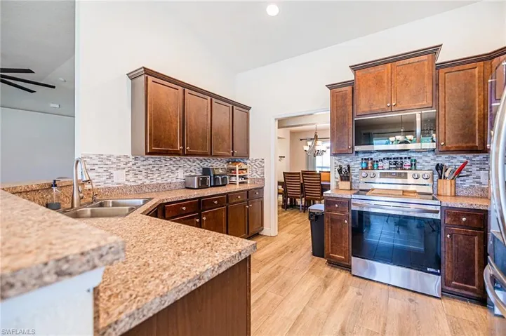 Kitchen with sink, light hardwood / wood-style flooring, stainless steel appliances, decorative backsplash, and ceiling fan