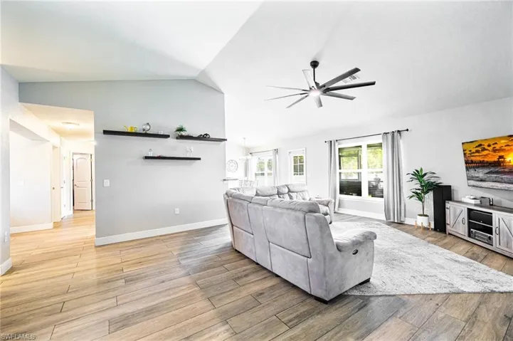 Living room with light hardwood / wood-style floors, vaulted ceiling, and ceiling fan