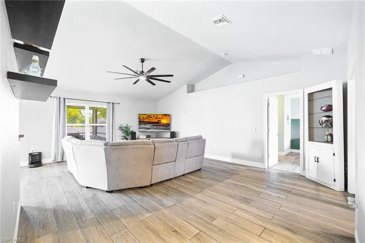 Living room with lofted ceiling, ceiling fan, and light hardwood / wood-style floors